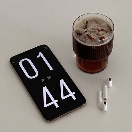 Un móvil marcando la 1:44 de la tarde junto a un café con hielo y unos auriculares, sobre una mesa.