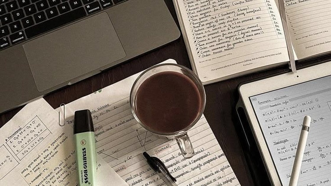 Un escritorio con un portátil, una libreta con una lista escrita a mano y una taza de café.